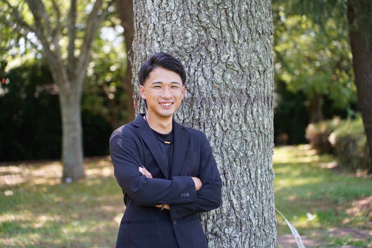 樹木のそばで微笑む株式会社STG代表取締役 澤田叶夢